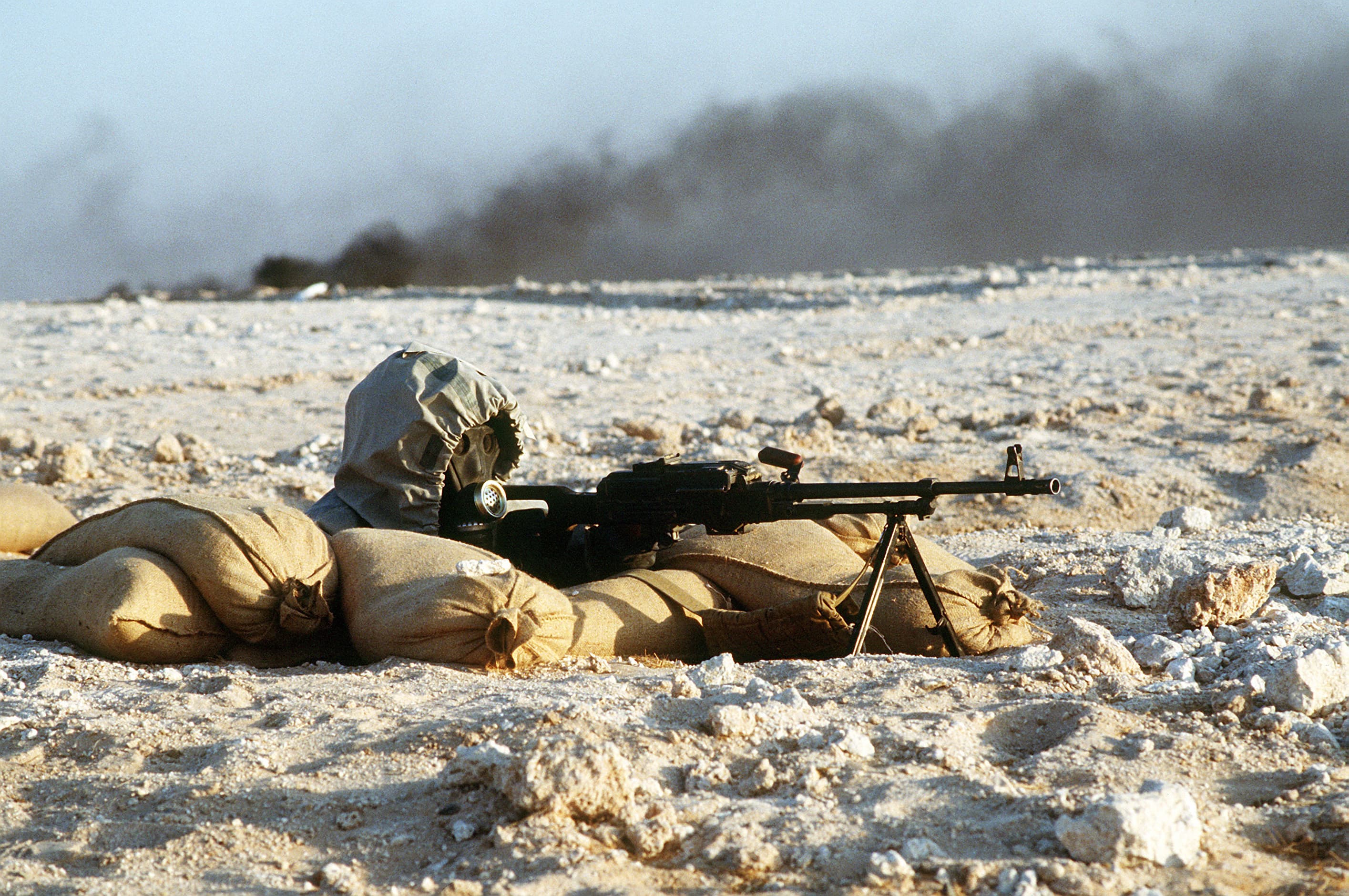 A Hive gunner sights his PKM as The People's Teeming burns in the background.